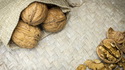 Beautiful arrangement of walnut shells in burlap sack and walnut kernels on light wicker surface. Copy space in middle.