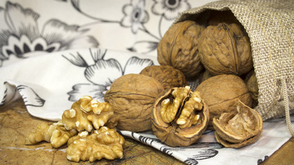 Walnut shells and walnuts kernels in burlap sack on top of marble countertop with white towel with flowers.