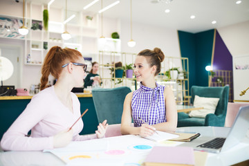 Obraz premium Cheerful pretty women brainstorming and looking at each other at desk with papers
