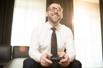 From below shot of happy adult businessman relaxing and playing videogame with gamepad looking away © pressmaster