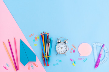 Back to school styled flat lay scene with multicolored school supplies with paper plane on pink and blue background with copy space