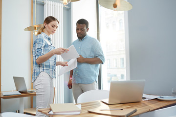African-American man and young woman looking at important documents while standing in modern office together