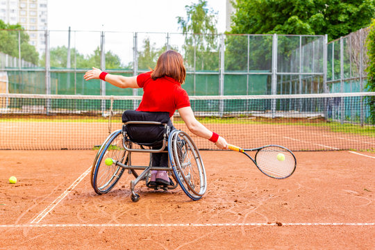 Disabled young woman on wheelchair playing tennis on tennis court.