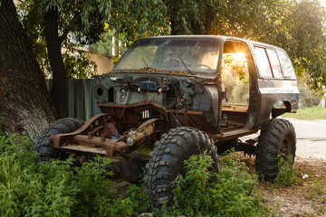 Close-up of an old rusty jeep car with a broken door and no wheels on the background of a green coniferous forest