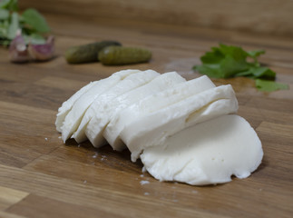 Sliced mozzarella served on a wooden cutting board with vegetables in the background