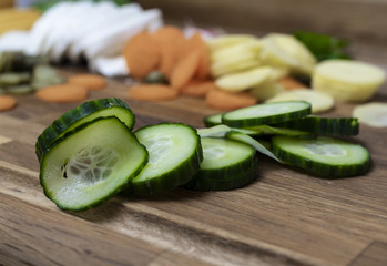Slices of cucumber on a wooden cutting board with other ingredients in the background.