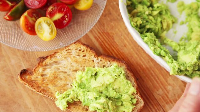 A woman makes avocado toast with cherry tomatoes and bacon