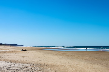Sunshine Coast beach in Australia with unreognizable people silhouetted in the distance, including one man on a laptop