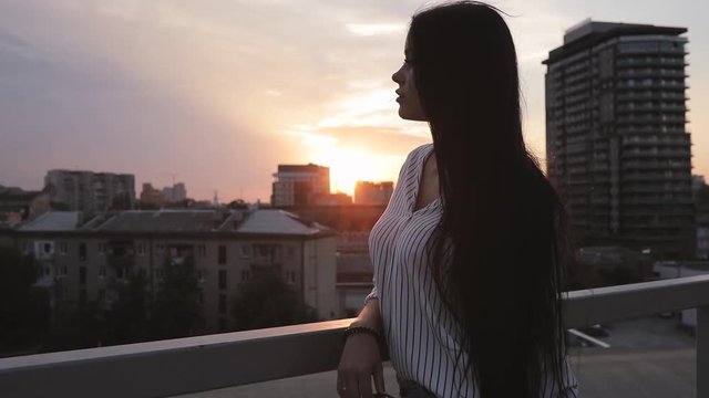 Young woman looking to cityscape from rooftop in sunset time