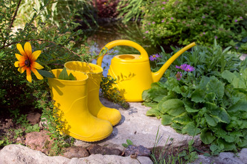 Yellow children's rubber boots with flower and yellow garden watering can on a background with a...