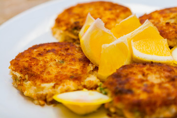 Close-up of Crispy Crab and Fish Cakes with Lemon Wedges on a White Plate