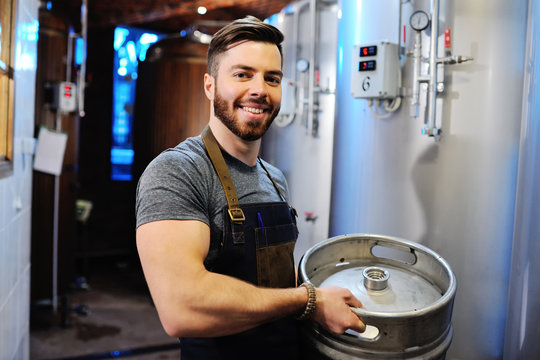 Male brewer with a metal beer barrel on the background of the brewery - Powered by Adobe