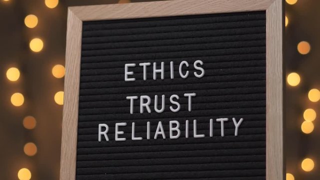 Black letter board with ETHICS TRUST RELIABILITY Written on it with white letters. Camera rotating around the sign showing the beautiful bokeh balls in the background.