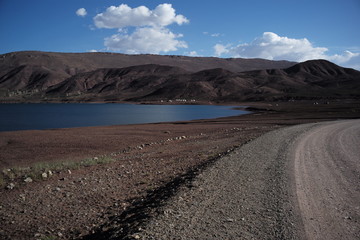 road along bank of a mountain lake with blue sky and clouds