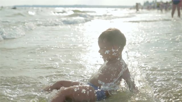 A small, cheerful, happy boy is swimming in the sea. He runs, jumps and splashes.