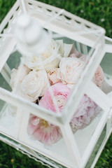 Pink flowers in white retro lantern on green grass, elegant floral decoration–