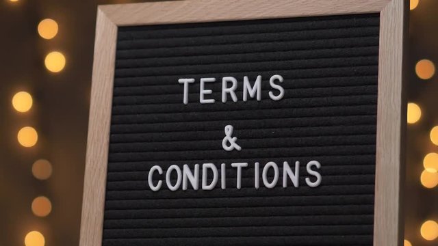 Black letter board with TERMS & CONDITIONS Written on it with white letters. Camera rotating around the sign showing the beautiful bokeh balls in the background.