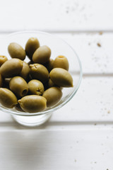 Pile of delicious green olives in small glass bowl on white background