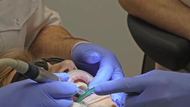 Dentist is treating patient in modern dental office. Orthodontist works with an assistant. In operation, cofferdam is used. The client is make denture. Doctor and assistant work in protective masks.