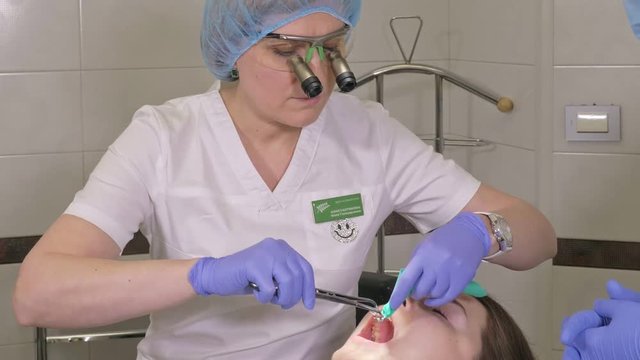Woman at dentist clinic gets dental treatment to fill a cavity in a tooth. Dental restoration and composite material polymerization with UV light and laser. Installation of dental dam.