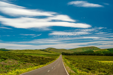 A road in the middle of some green fields with blue sky and some clouds in Flores Island in Azores