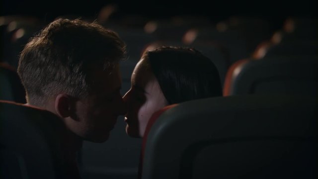 Love couple alone at empty cinema hall. Young guy and girl kissing in movie theatre. Cinema couple in love. Romantic date in movie theater. Kissing couple in slow motion