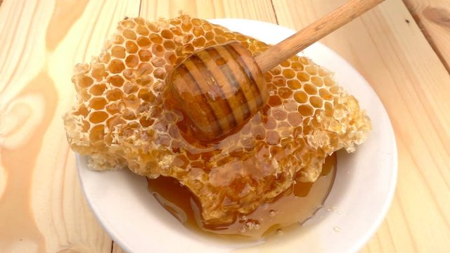 Honey dripping from honey dipper on honeycomb, over yellow background. slow motion