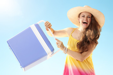 happy young woman with blue plastic cooler box against blue sky