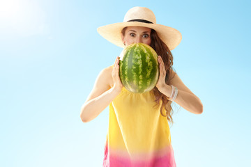 surprised woman looking out from watermelon against blue sky
