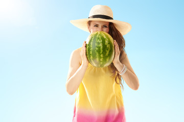 happy woman looking out from watermelon against blue sky