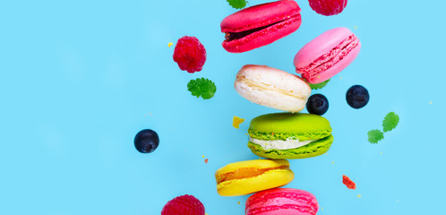 Assorted macaroons falling cookies with berries close up on blue background banner