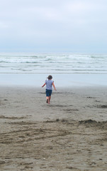 Fototapeta na wymiar Small, Cute, 6 years Girl, Brown hair, playing in the water, running, Pacific Ocean, Oregon coast, family vacation time, reflection in the water