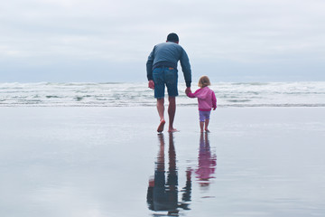 man and toddler girl walking on the beach