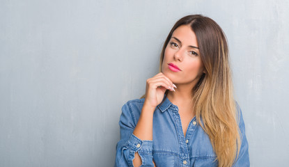 Young adult woman over grunge grey wall wearing denim outfit with hand on chin thinking about question, pensive expression. Smiling with thoughtful face. Doubt concept.