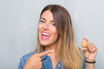 Young adult woman over grey grunge wall showing dried walnut very happy pointing with hand and finger