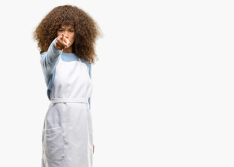 African american shop owner woman wearing an apron pointing to the front with finger