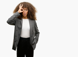 African american business woman wearing glasses doing ok gesture shocked with surprised face, eye looking through fingers. Unbelieving expression.