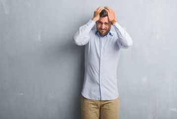 Handsome young business man over grey grunge wall wearing elegant shirt suffering from headache desperate and stressed because pain and migraine. Hands on head.