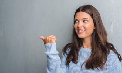 Young brunette woman over grunge grey wall pointing and showing with thumb up to the side with happy face smiling