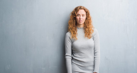 Young redhead woman over grey grunge wall with a confident expression on smart face thinking serious