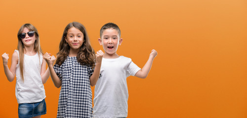 Group of boy and girls kids over orange background screaming proud and celebrating victory and success very excited, cheering emotion