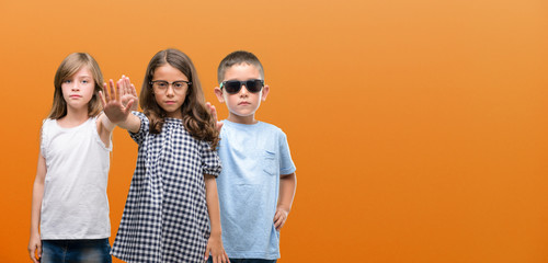 Group of boy and girls kids over orange background with open hand doing stop sign with serious and...