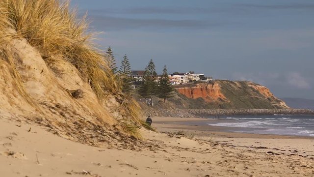 Grandfather with grandson walking along Christies Beach in South Australia. Sand dunes and cliff tops visible.