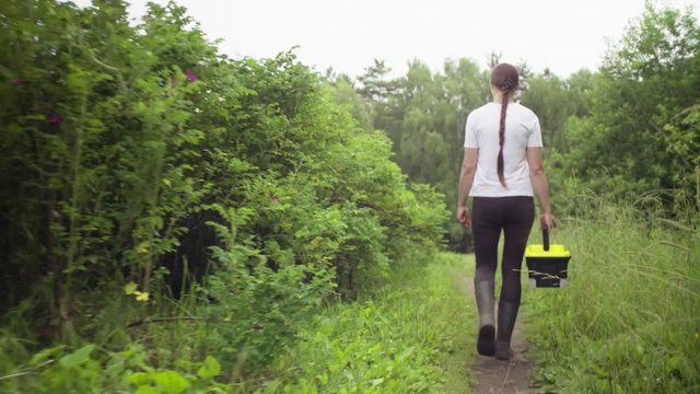 Dolly shot. The woman scientist environmentalist with the tool box in her hand going to the place of research on a forest path. Rear view.