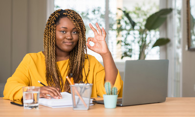 African american woman studying with laptop doing ok sign with fingers, excellent symbol