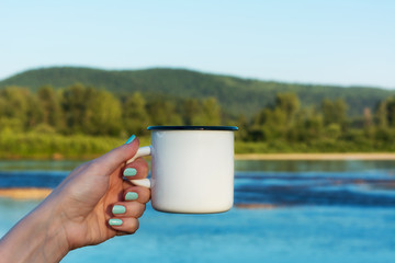 Woman holding enamel mug with river view