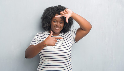 Young african american plus size woman over grey grunge wall smiling making frame with hands and fingers with happy face. Creativity and photography concept.