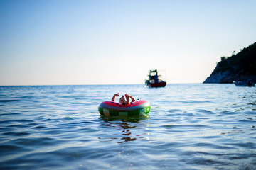 Little teen boy swims on an air mattress in the sea