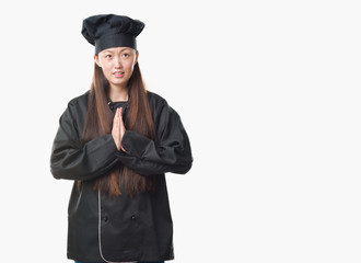 Young Chinese woman over isolated background wearing chef uniform begging and praying with hands together with hope expression on face very emotional and worried. Asking for forgiveness. Religion.