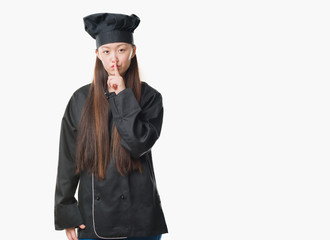 Young Chinese woman over isolated background wearing chef uniform asking to be quiet with finger on lips. Silence and secret concept.